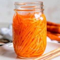 a glass jar filled with orange colored noodles next to chopsticks on a white plate