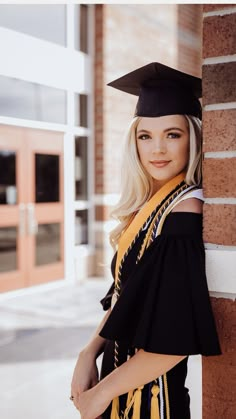 a woman wearing a graduation cap and gown leaning against a brick wall in front of a building