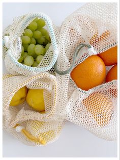 three mesh bags filled with fruit on top of a white tablecloth covered counter next to oranges, grapes and lemons