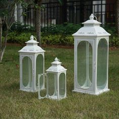 three white lanterns sitting on top of a lush green field