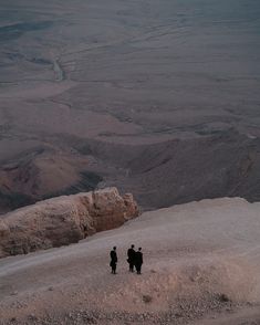 two people standing on top of a mountain looking down at the valley below them with mountains in the background