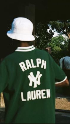 a man in a green shirt and white hat is looking at an elephant behind him