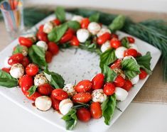 a white plate topped with tomatoes and mozzarella cheese covered in leaves on top of a table