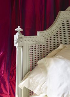 a bed with white sheets and pillows in front of a red curtain