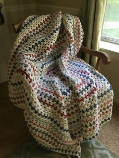 a crocheted blanket sitting on top of a wooden chair next to a window