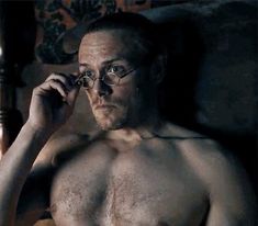 a shirtless man with glasses talking on a cell phone