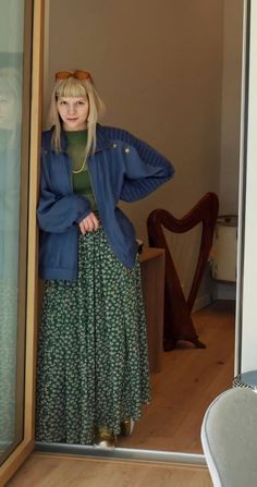 a woman standing in front of a door wearing a blue jacket and green floral skirt