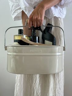 a woman is holding a white bucket filled with bottles and other household care products in her hands