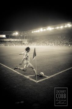 a young man kicking a soccer ball on top of a lush green field at night