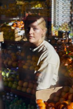 a woman is standing in front of a fruit stand with oranges and other fruits