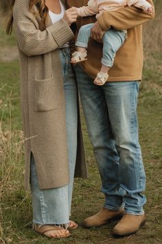 a woman holding a baby and standing next to a man in a brown cardigan