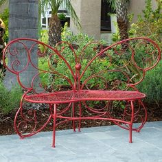 a red bench sitting on top of a sidewalk next to trees and bushes with palm trees in the background