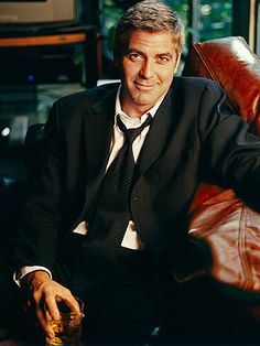 a man in a suit and tie sitting on a leather chair with his legs crossed