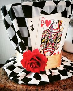 a red rose sitting on top of a black and white checkerboard hat with playing cards