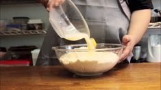 a person pouring batter into a bowl on top of a wooden table in a kitchen