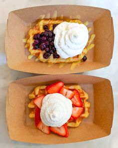 two waffles with strawberries, blueberries and whip cream on top are sitting in cardboard boxes