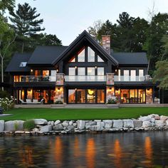 a large house sitting on top of a lush green field next to a lake and forest