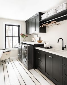 a washer and dryer in a very clean room with black cabinets, white flooring and a large window