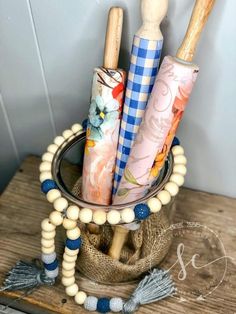 several wooden utensils are in a glass container on a wood table with beaded bracelets