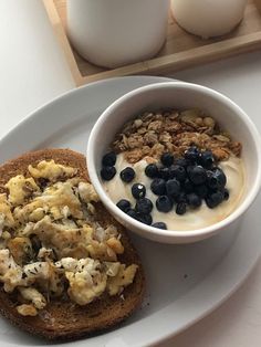 a white plate topped with an open face sandwich next to a bowl of yogurt