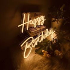 a happy birthday neon sign sitting on top of a fur rug next to a plant