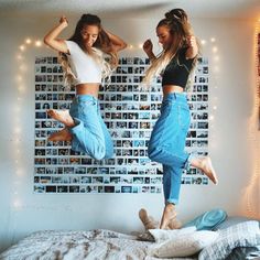 two girls jumping on a bed with their arms in the air and one girl is wearing jeans