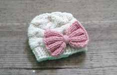 a crocheted hat with a pink bow on the side sitting on a wooden surface