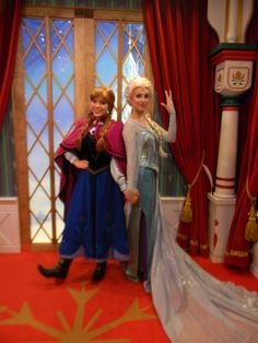 two frozen princesses posing for a photo in front of a window with red curtains