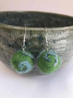 two balls of yarn sitting on top of a green bowl with silver earwires