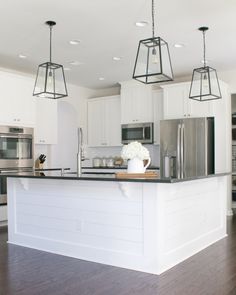 a kitchen with white cabinets and stainless steel appliances, including an island in the middle