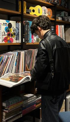 a man reading a book in front of a bookshelf full of cds and records