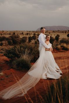 a bride and groom standing in the middle of an outback desert landscape with their veil blowing in the wind