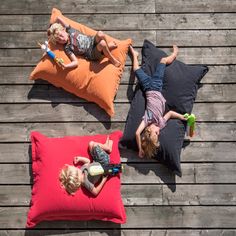 two young children laying on pillows on a wooden deck