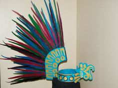 a colorful headdress made out of feathers on top of a black vase in front of a white wall