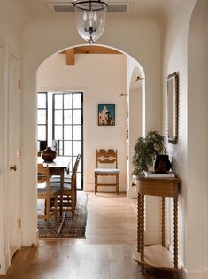 an archway leading to a dining room and living room area with wood floors, white walls and wooden furniture