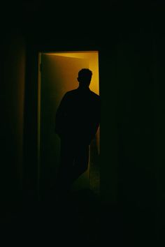 a man standing in front of a doorway with his back turned to the camera, at night