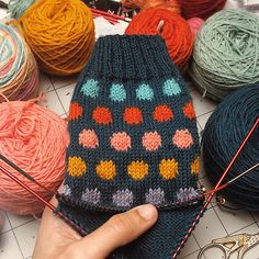 a hand is holding up a knitted mitt next to balls of yarn and scissors