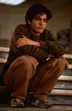 a young man sitting on top of a wooden bench in front of some stairs with his arms crossed