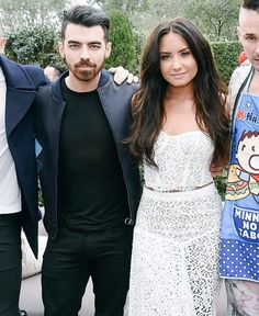 three people standing next to each other in front of trees and bushes at an event