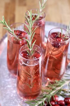 three glasses filled with wine and garnished with rosemary sprigs on a tray