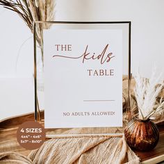 there is a sign that says the kids table and two vases with feathers on it