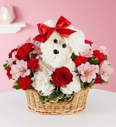 a teddy bear sitting in a basket filled with red and white flowers on a table