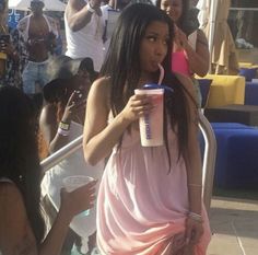 a woman in a pink dress drinking from a plastic cup while standing next to other people