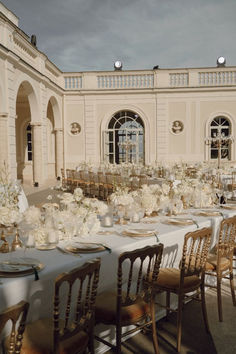 the tables are set with white flowers and place settings for an elegant wedding reception in front of a large building