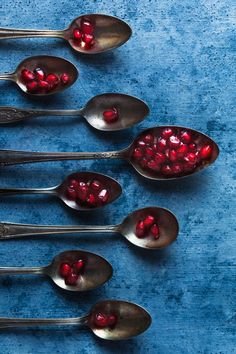 six spoons with pomegranate in them on a blue surface