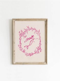 a pink and white drawing of a mermaid in a frame on the wall above a toilet