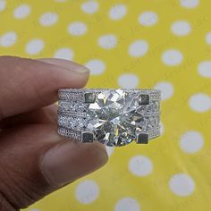 a hand holding a diamond ring in front of a yellow background