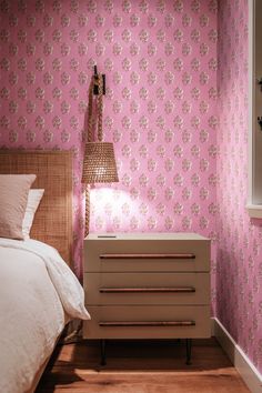 a bedroom with pink wallpaper and a white bed in front of a nightstand next to a window