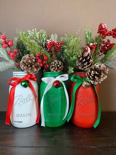 three mason jars decorated with pine cones and holly