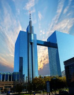 two tall buildings in front of a blue sky with clouds and sun shining through them